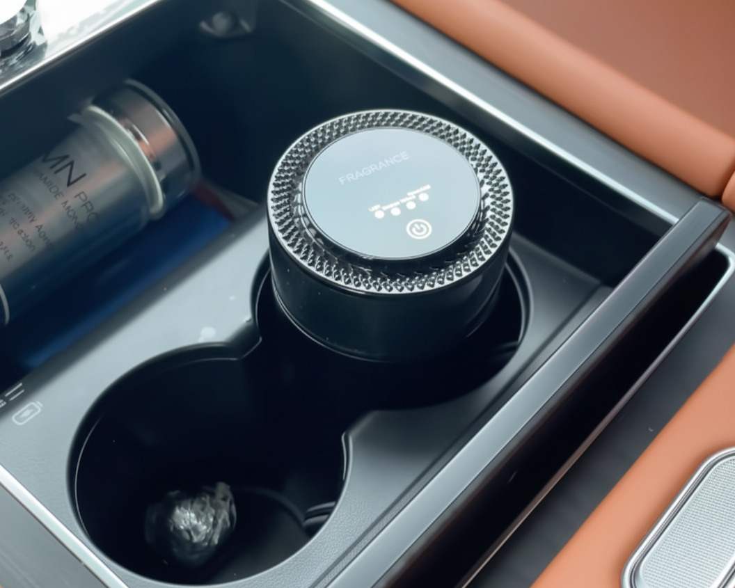 Car cup holder with a black air freshener and a bottle of perfume.